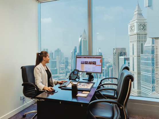 A professional woman working at her desk in a modern Servcorp private office, with a stunning panoramic view of Dubai’s skyline, at Almas Tower, Dubai