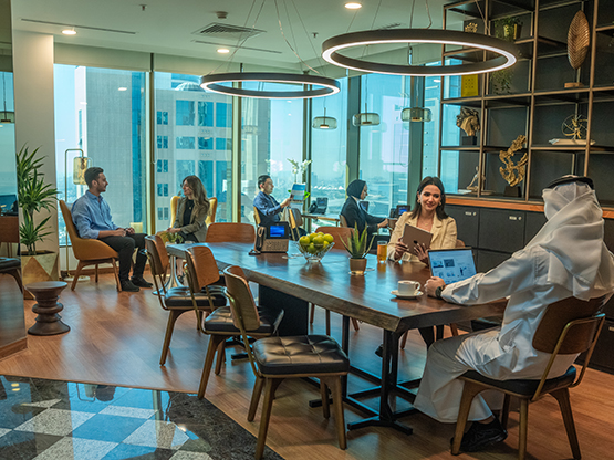  A dynamic shared workspace at Sahab Tower, Kuwait, where professionals collaborate and work individually in a bright, modern setting with large windows offering city views.
